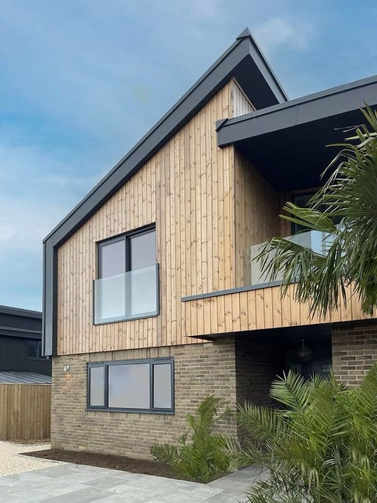 Modern two-storey house with wood siding and palm trees at Headon Reach, showing luxury timber frame homes on the Isle of Wight.