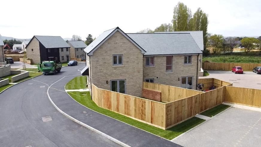 Aerial view of a modern suburban neighbourhood at Branstone Farm featuring a two-storey brick house within the affordable timber frame housing layout.