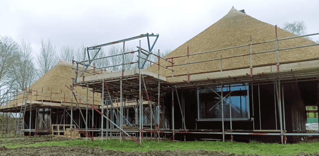 Thatched-roof houses under construction with scaffolding for a net zero self-build timber frame design project.